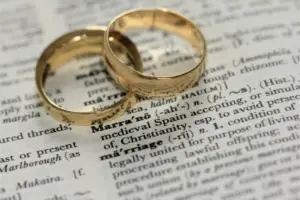 Zwei goldene Eheringe liegen auf der aufgeschlagenen Wörterbuchseite mit der Definition des englischen Begriffs „marriage“.